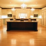 Overview of neoclassical kitchen with white cabinetry, kitchen island, hardwood floor and decorative chandeliers