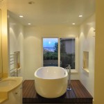 bathroom with white cabinetry, oval white tub sitting on wood stage and wall niche