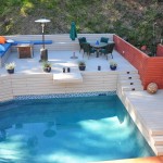 Overview of exterior pool with trex deck with sitting area and umbrella and redwood fence